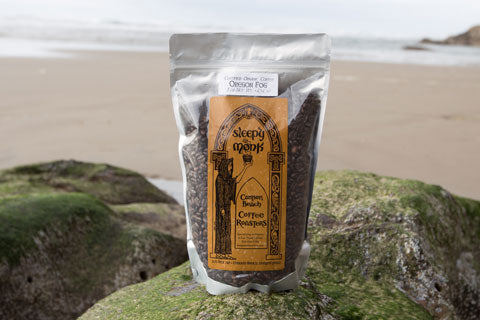 A bag of Oregon Fog Sleepy Monk Coffee sitting on a rock with seaweed 
